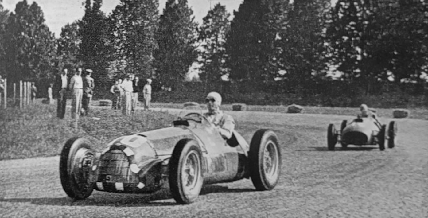 Black and white photograph of Giuseppe Farina in a white helmet driving an Alfa Romeo 159 on a gravel-edged bend at Monza, with a Ferrari following and spectators on the grass behind