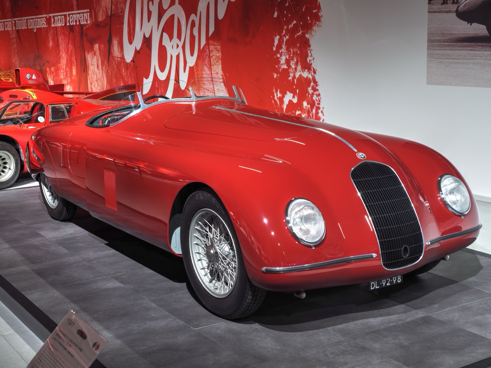 A red streamlined open two-seater with faired-in wings, a small oval grille and a wrap-round windscreen, on a museum floor