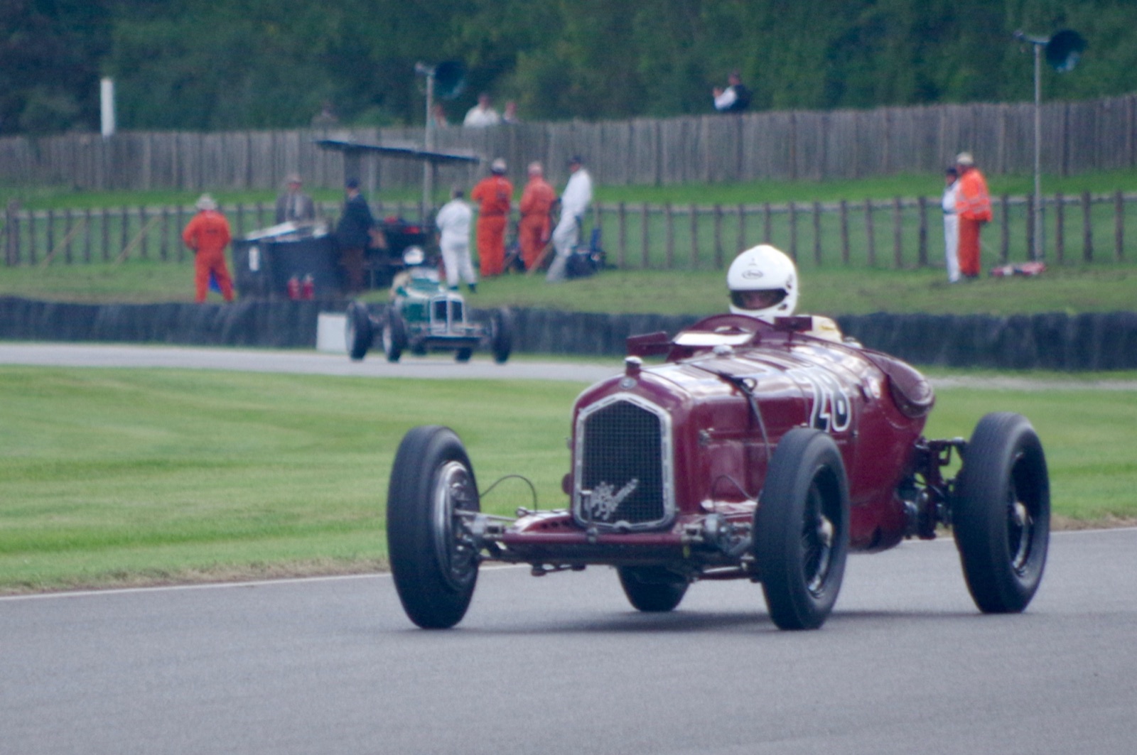 A dark red Alfa Romeo P3 numbered 28 cornering on a track with a driver in a white helmet, marshals in orange overalls behind