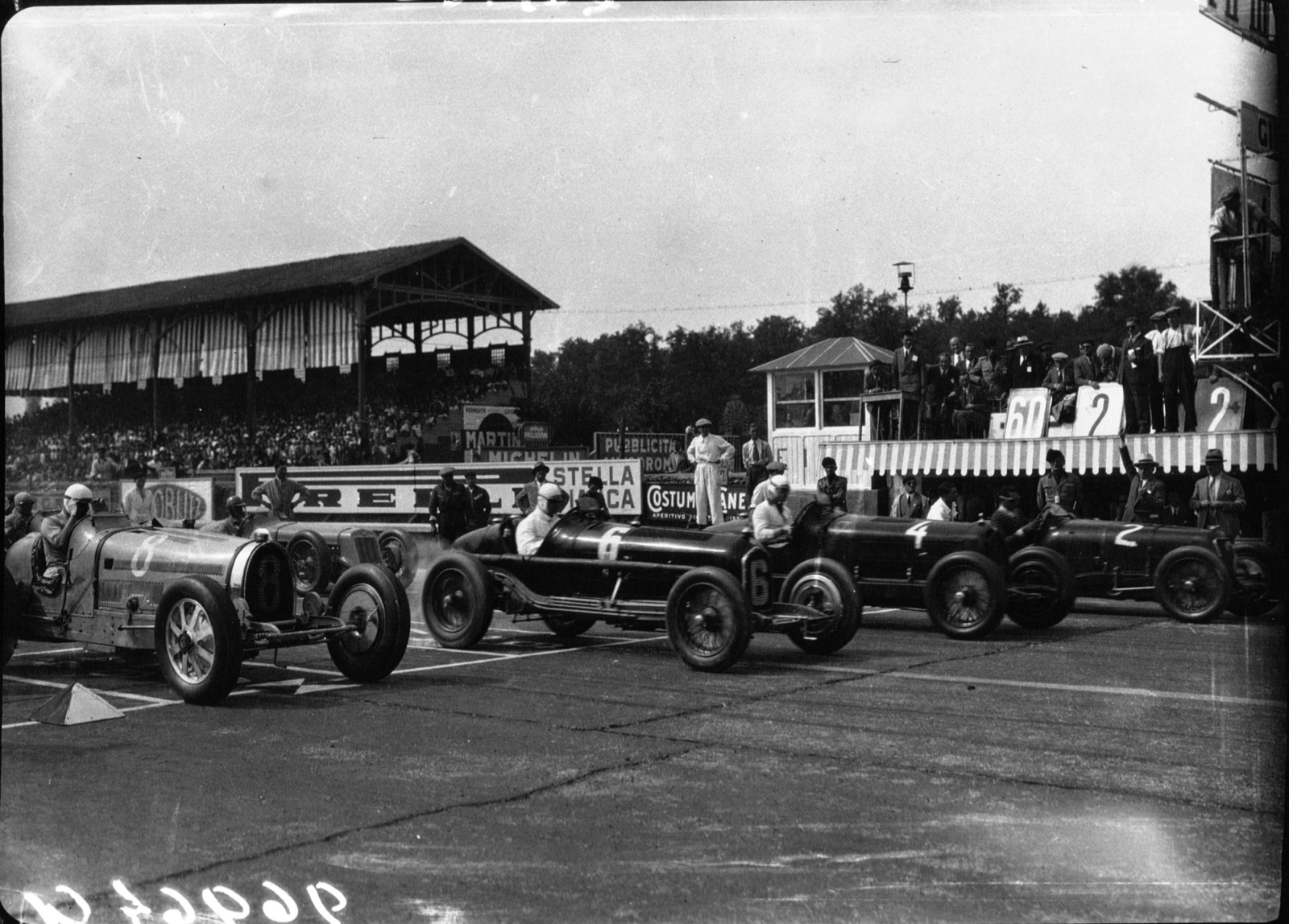Front row of the 1932 Monza Grand Prix: a Bugatti on the left and black Alfa Romeo single-seaters numbered 6, 4 and 2, with a grandstand behind