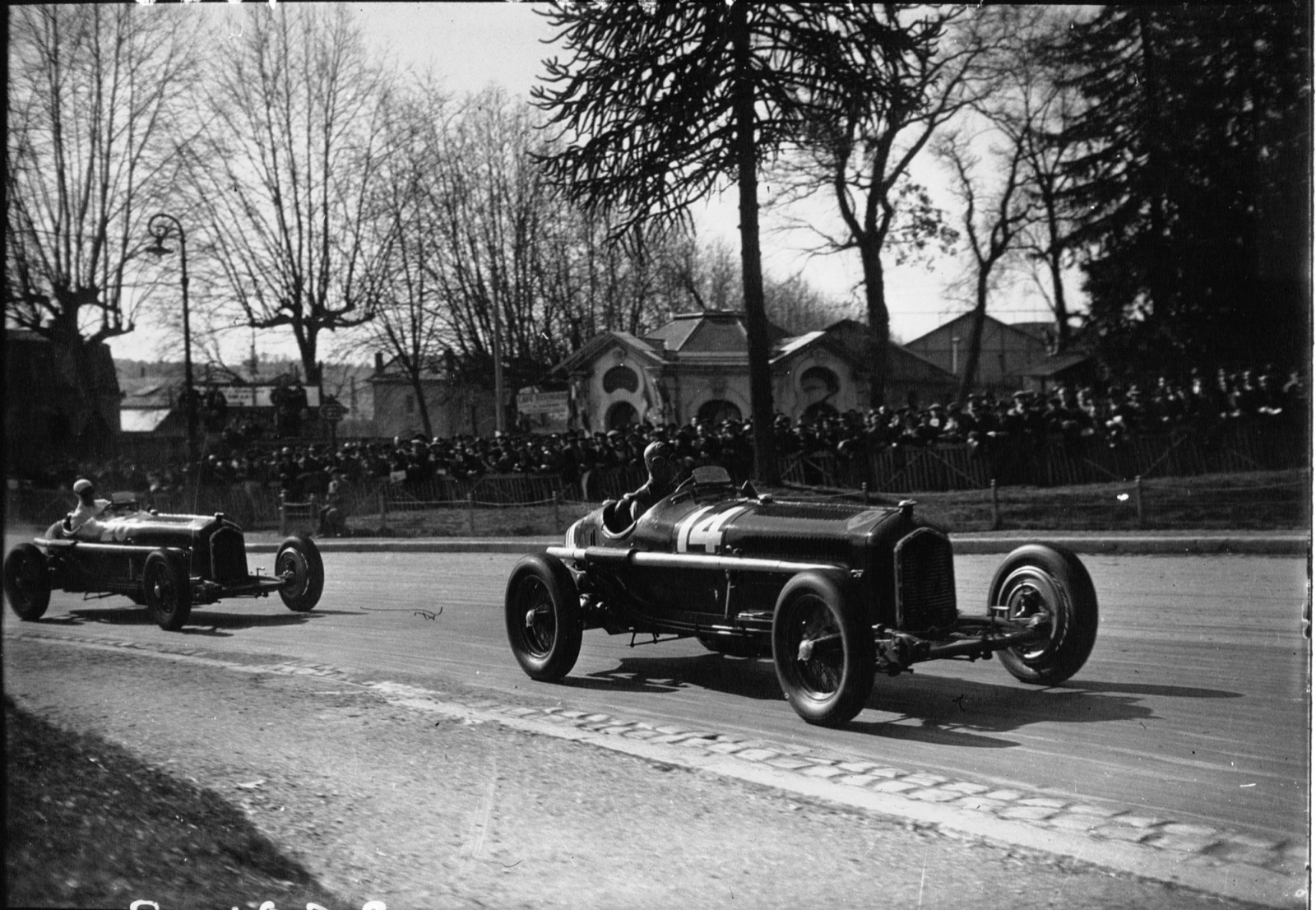 Two dark Alfa Romeo P3s racing on a tree-lined street past a crowd, the nearer car numbered 14