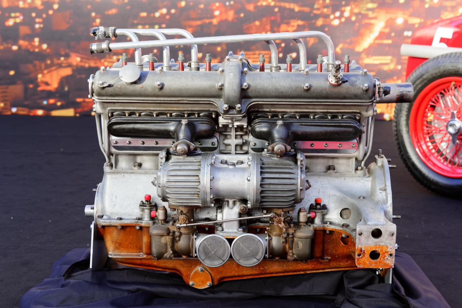 An Alfa Romeo Tipo B straight-eight engine on a stand, seen from the supercharger side, with the twin finned superchargers and two carburettor intakes below the long cam cover