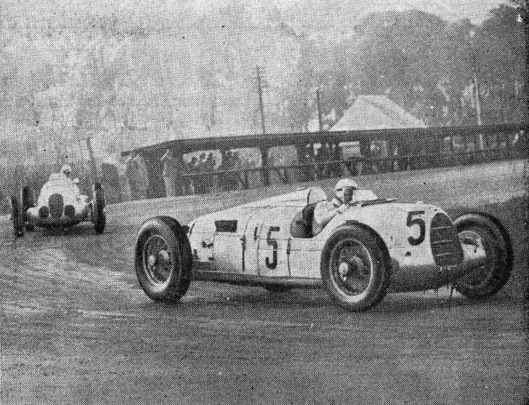 Rosemeyer's white Auto Union number 5 leads a Mercedes through a corner past a wooden footbridge at Donington Park