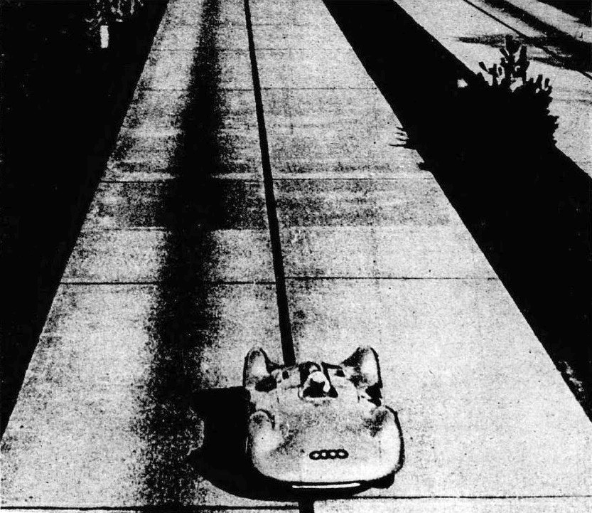 A streamlined Auto Union seen from above and ahead on an empty concrete autobahn, with its long shadow and the four-ring badge on the nose