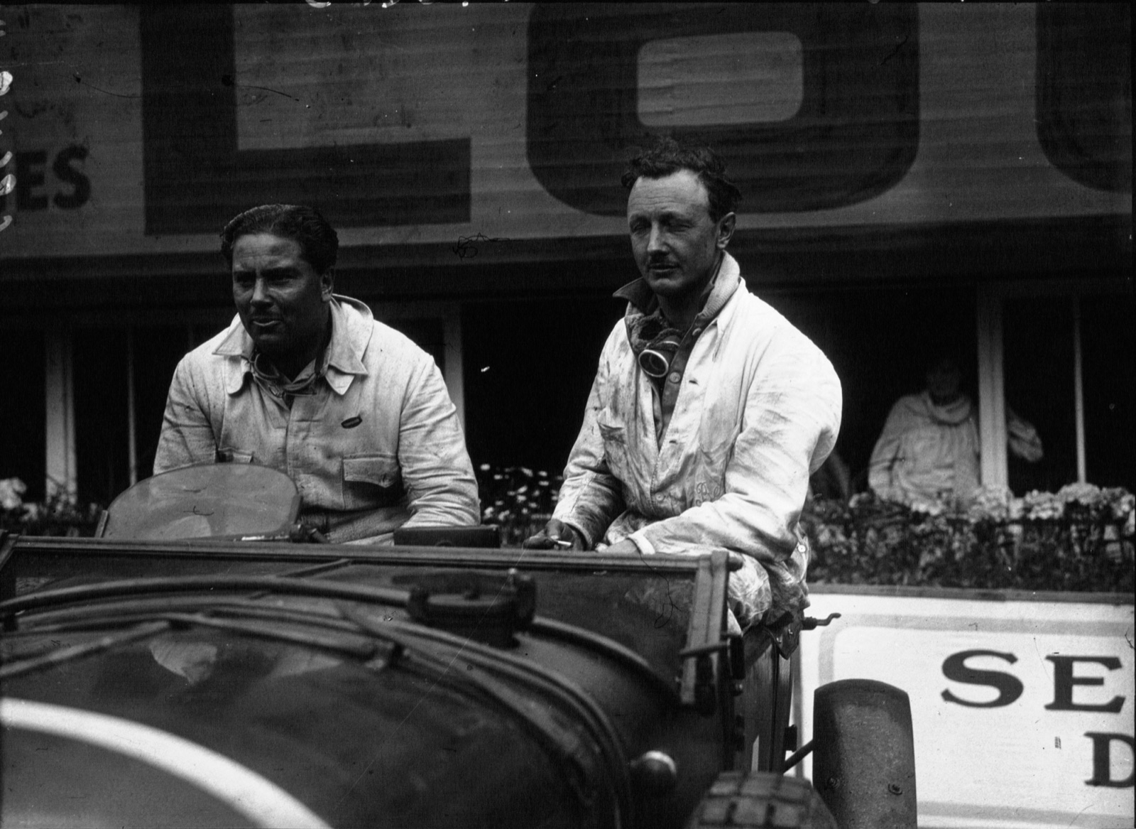 Woolf Barnato and Tim Birkin in white overalls sitting in their Bentley in front of the Le Mans pits in 1929