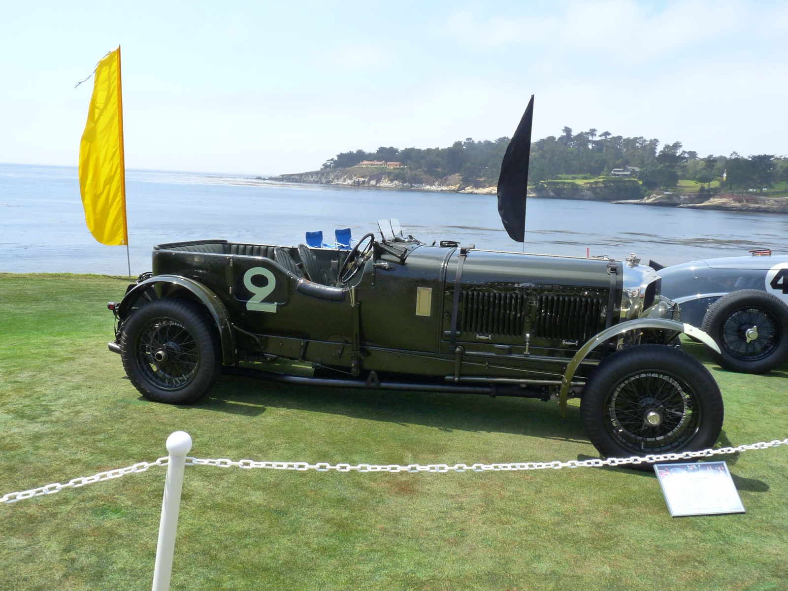 A dark green open Bentley Speed Six tourer with a white racing number 2 on its side, parked on grass by the sea at Pebble Beach