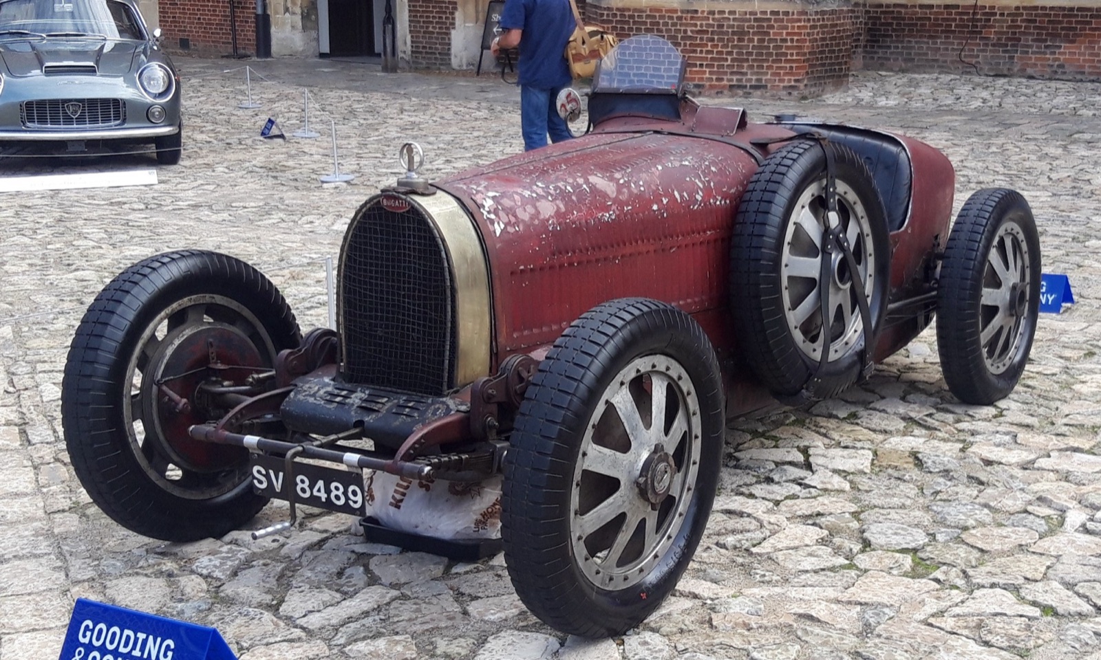 Red Bugatti Type 35C with worn, flaking paint and cast eight-spoke wheels on cobbles in a palace courtyard