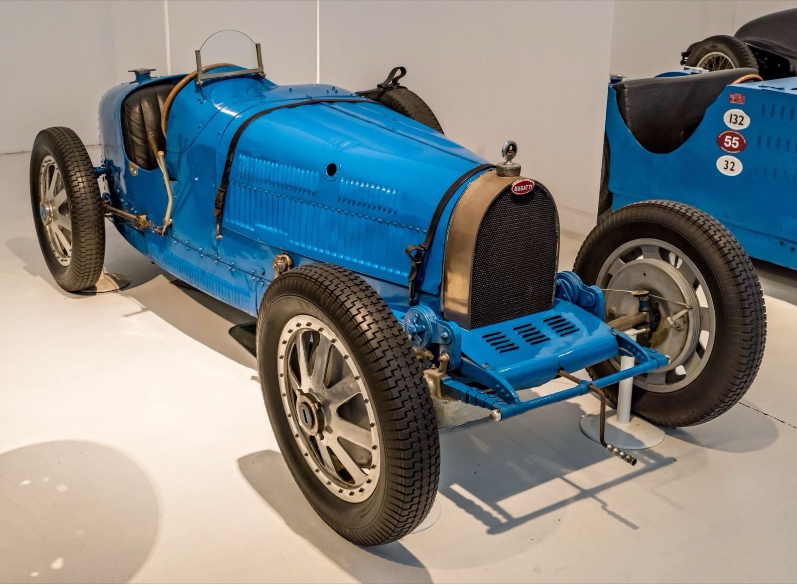 Blue Bugatti Type 35 two-seater with cast eight-spoke wheels and hollow front axle, in a museum hall