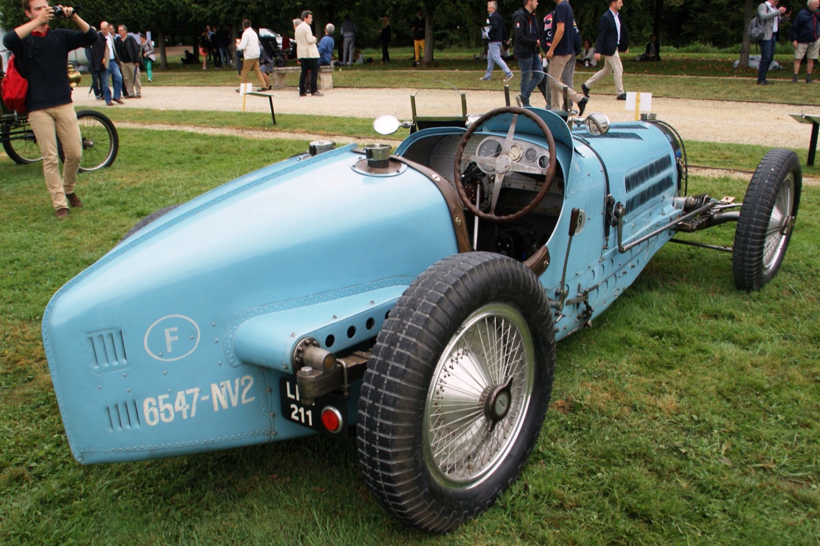 Rear three-quarter view of a pale blue Bugatti Type 59 on grass, with the French plate 6547-NV2 painted on its tail and an LPG 211 plate below