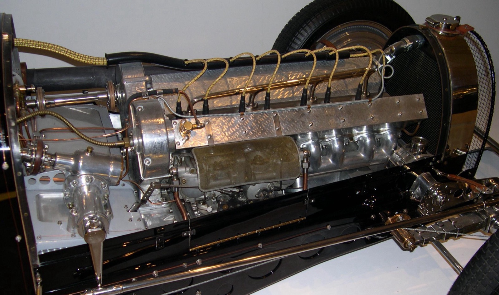 The polished straight-eight engine of a Bugatti Type 59 with the bonnet off, showing the cam covers, spark plug leads and the supercharger casing