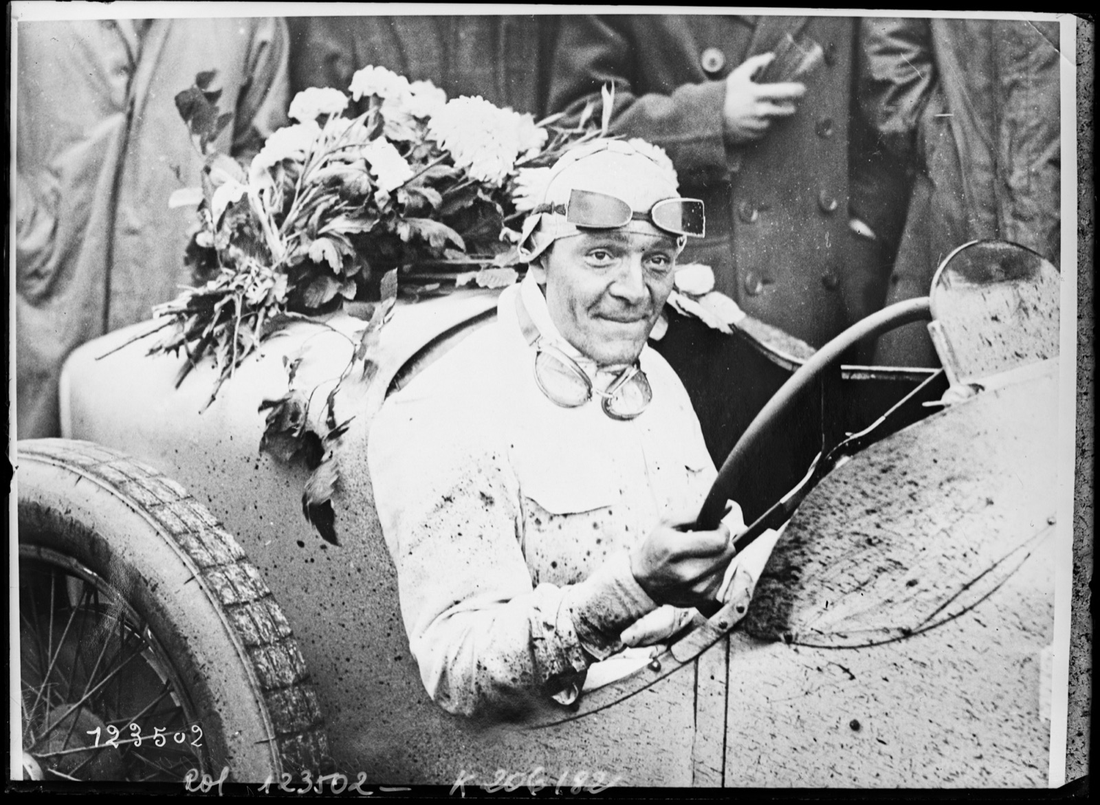 Robert Benoist in goggles and a mud-spattered overall at the wheel of his Delage, flowers laid on the scuttle