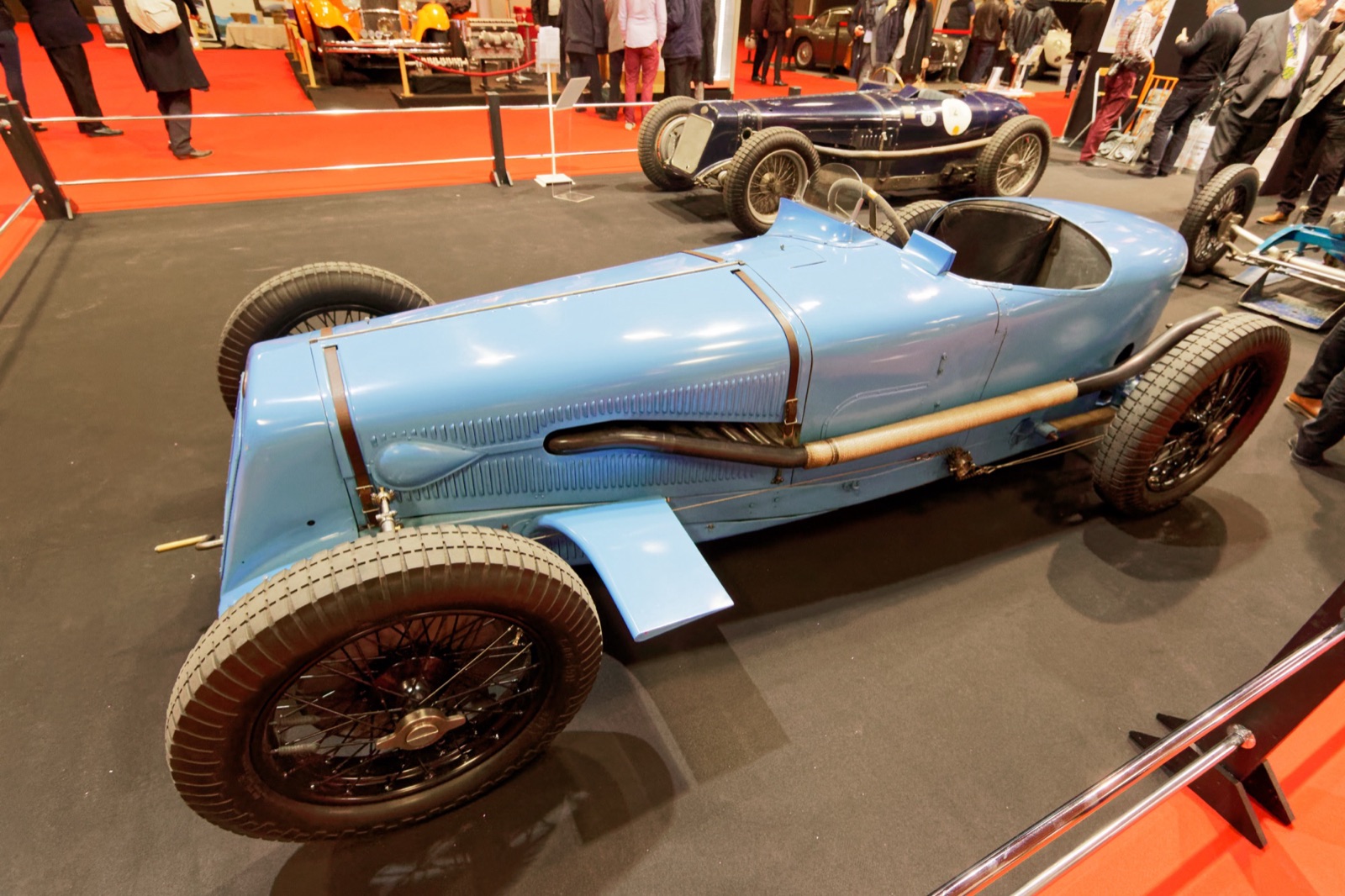 Light blue Delage 15 S8 single-seater with its exhaust pipe along the left side, on a stand at a Paris show