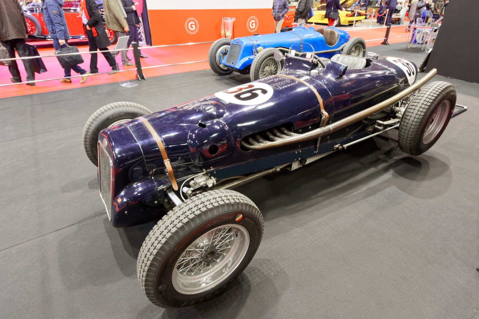 Dark blue single-seater numbered 36 with a long exhaust along its side, a light blue Delage behind it, at an indoor show