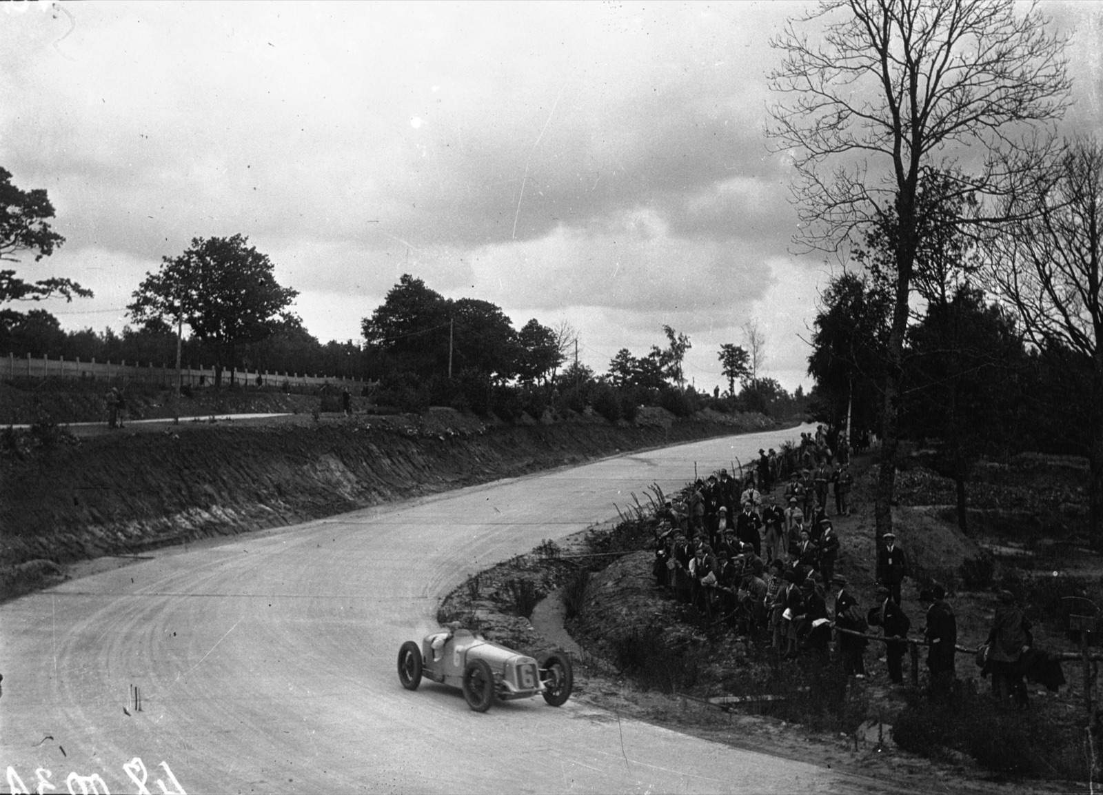 A Delage numbered 6 rounding a curve at Montlhéry with spectators lining the bank under trees