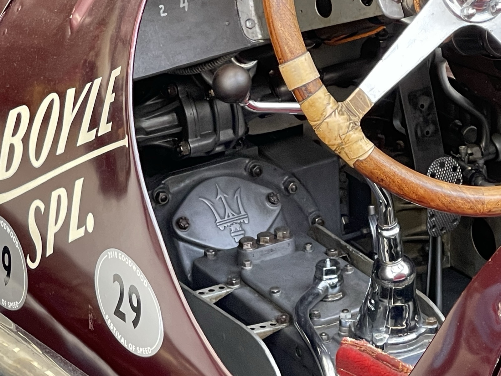 Side view into the cockpit of the dark red Maserati 8CTF Boyle Special, showing the wooden steering wheel, a chrome gear lever and a casing marked with the Maserati trident