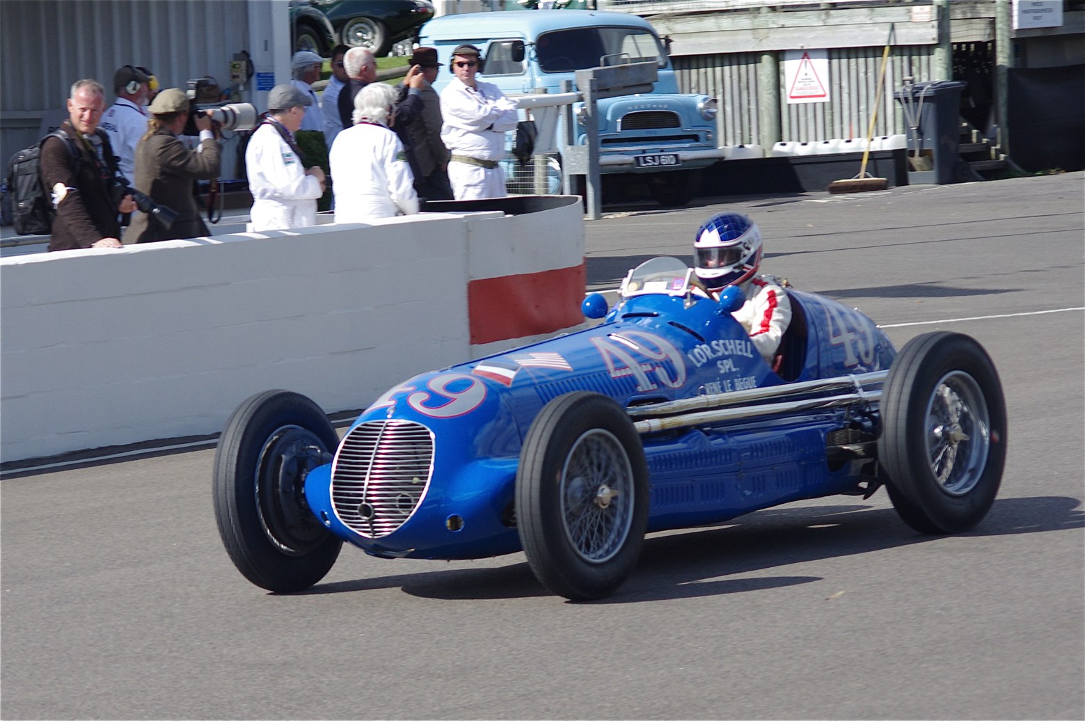 A blue Maserati 8CTF numbered 49 with French and American flags and the words L.O'R. Schell Spl. on the bodywork, being driven past a pit wall with photographers
