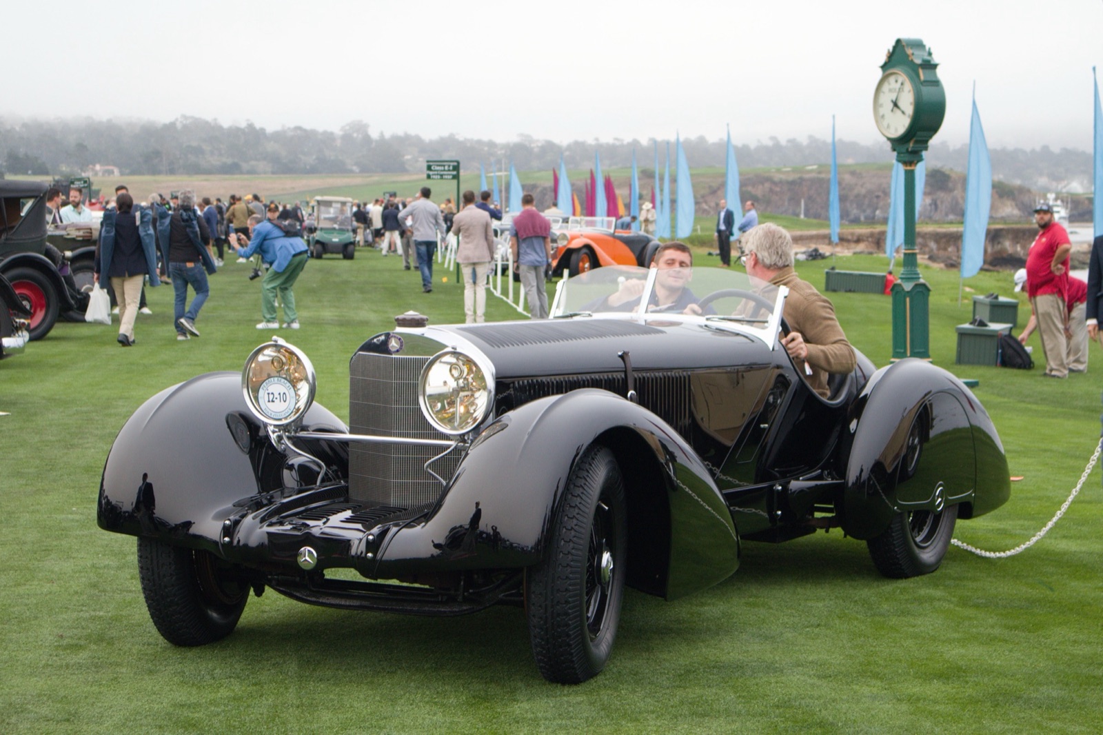 A long black Mercedes-Benz roadster with flowing wings, a tapered tail and a vertical grille, on the lawn at a concours with spectators behind