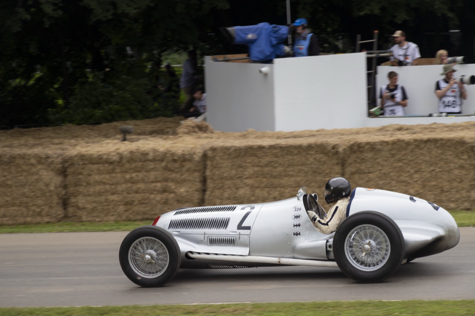 A silver Mercedes-Benz W125 driven past straw bales and photographers at the Goodwood Festival of Speed