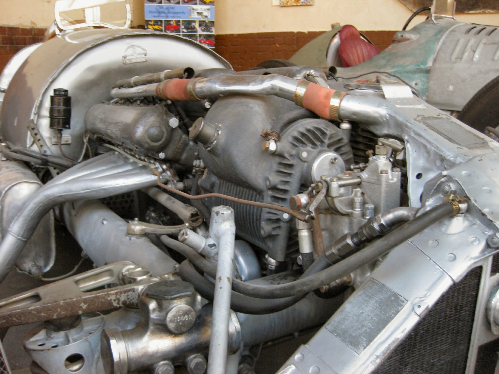Close view of the engine bay of a bare-metal Mercedes-Benz W154, with a large finned supercharger casing, exhaust pipes and fuel lines