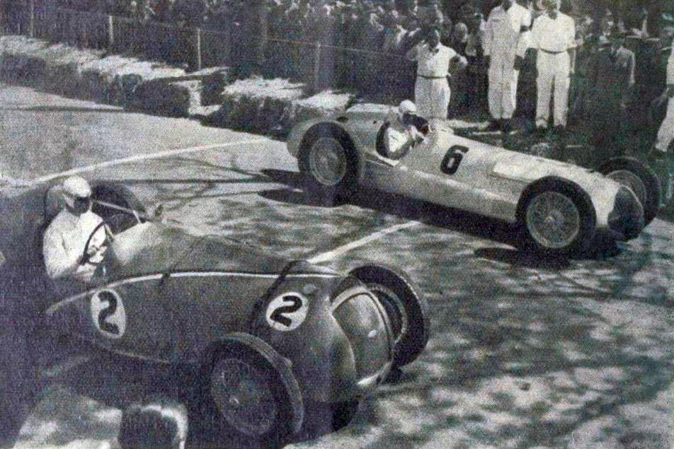 René Dreyfus in a dark Delahaye numbered 2 beside Rudolf Caracciola in a silver Mercedes-Benz W154 numbered 6 on a street circuit lined with straw bales