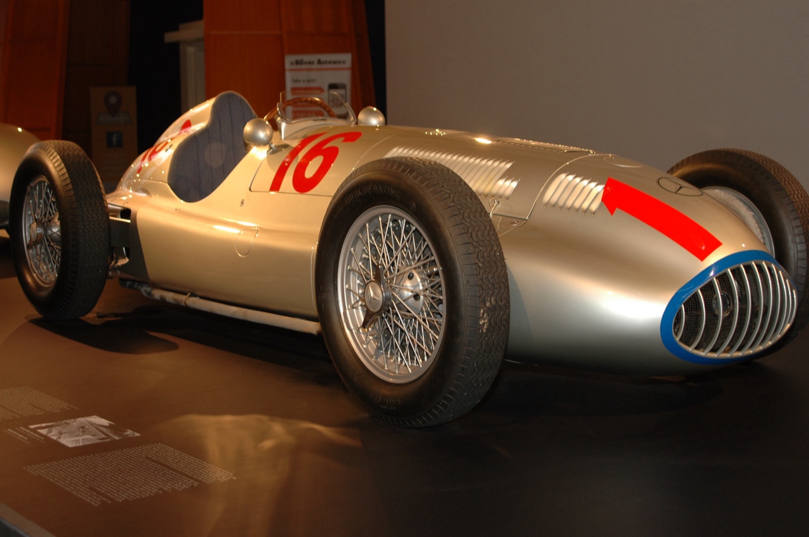 Front three-quarter view of a silver Mercedes-Benz W165 with a red 16 on the scuttle, a red arrow on the nose and a blue ring round the radiator grille