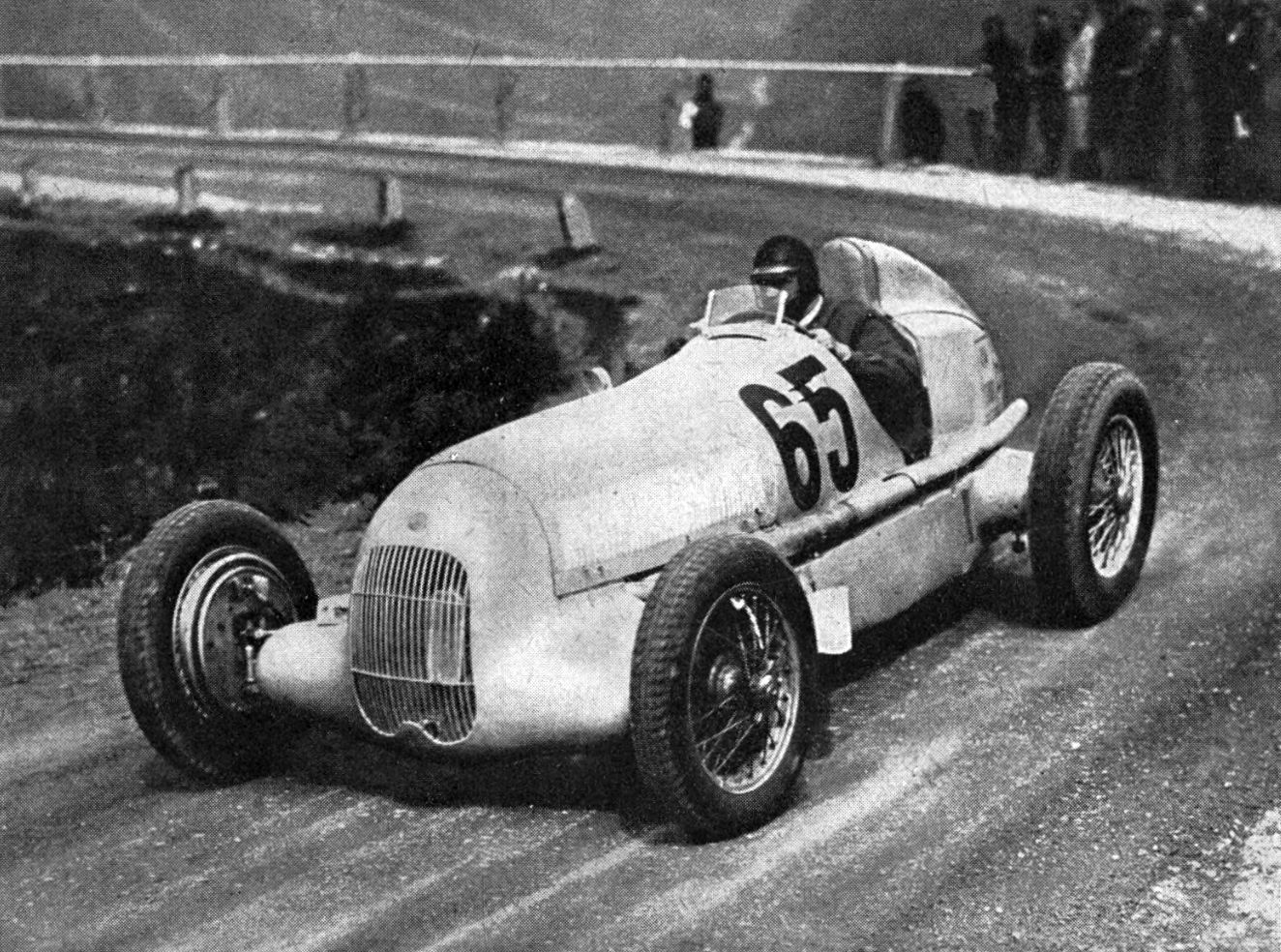Rudolf Caracciola in a Mercedes-Benz W25 numbered 65 rounds a bend on a gravel mountain road, spectators behind a fence