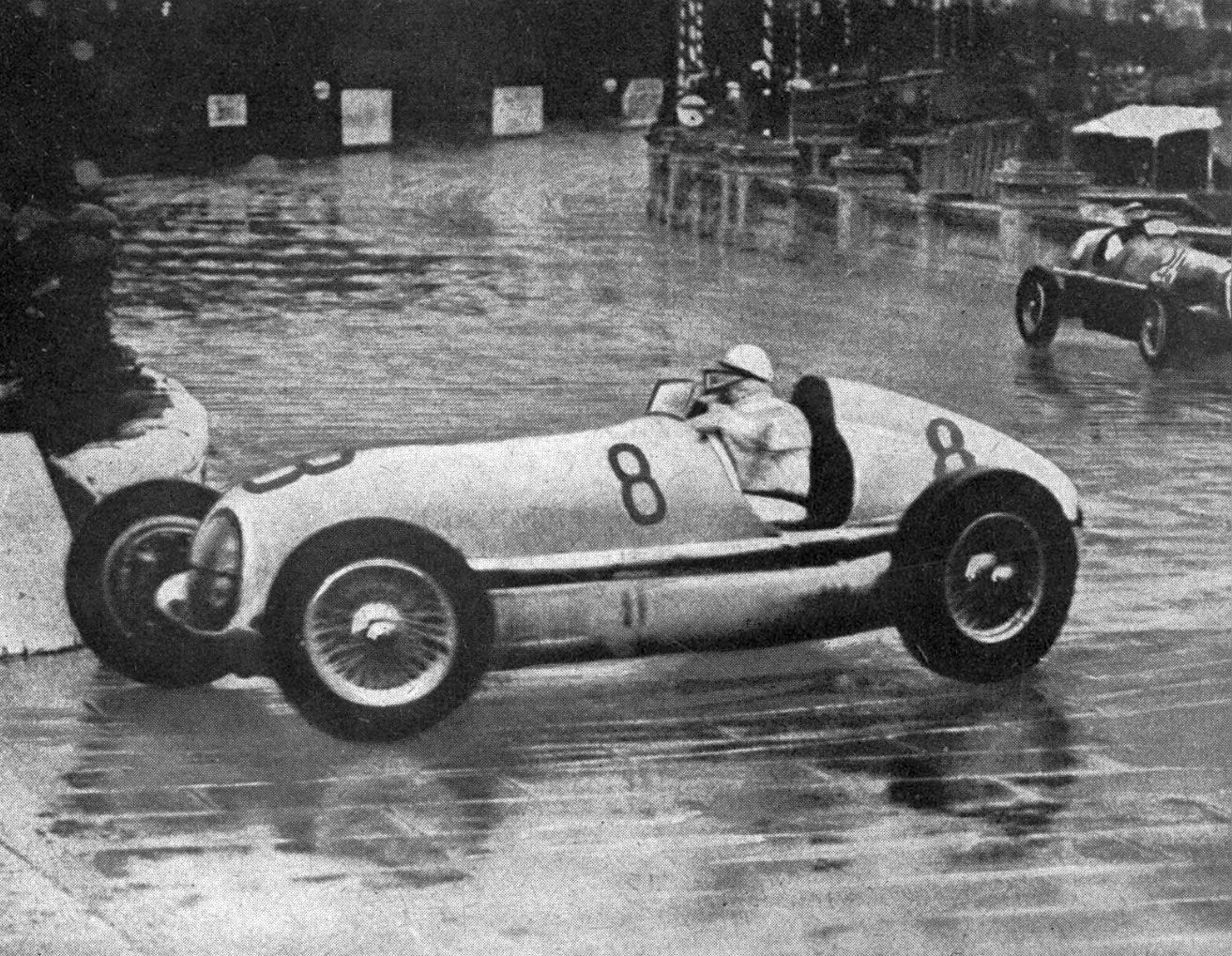 Caracciola's Mercedes-Benz W25 numbered 8 slides through a wet corner at Monaco, another car behind