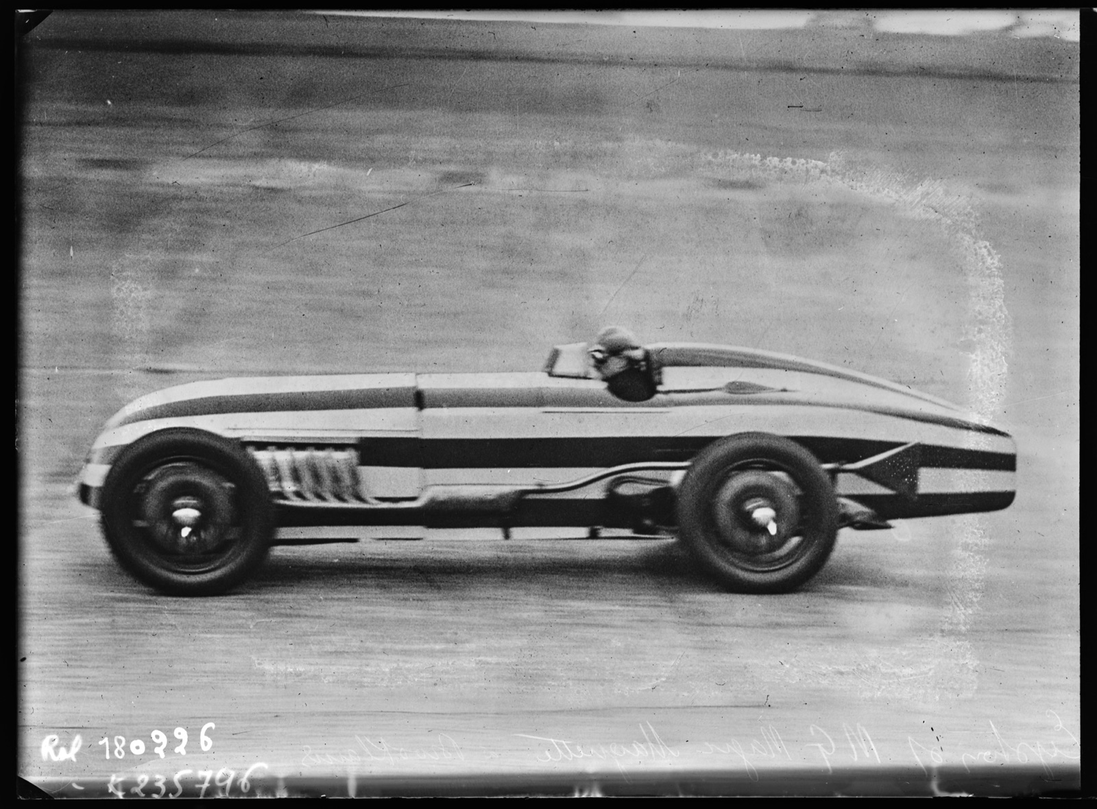 Side view of Eyston's single-seater MG Magic Magnette at speed on the Brooklands concrete, its long striped body and head fairing blurred by motion