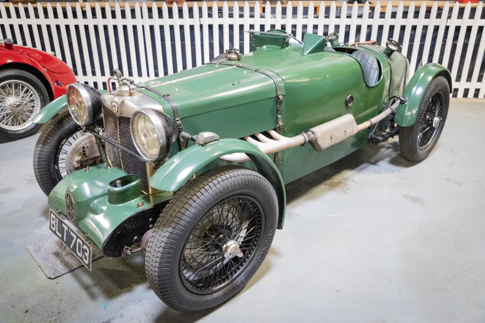 Green MG K3 Magnette registered BLT 703, with cycle wings, a side exhaust and worn original paint, on display beside a white picket fence