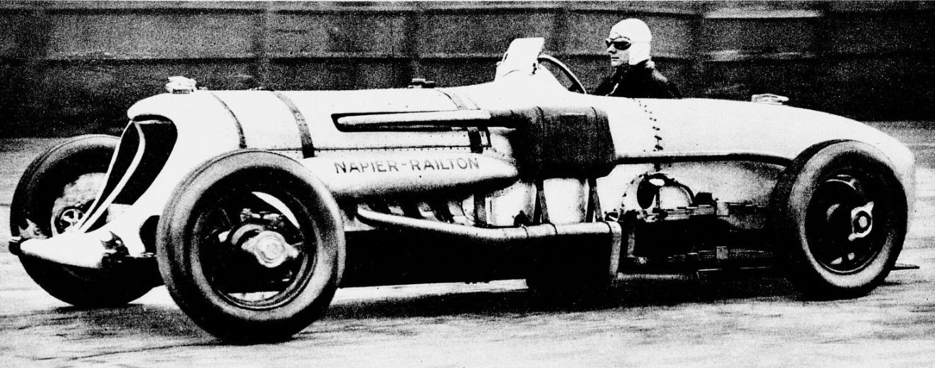 Period newspaper photograph of John Cobb in goggles and a white helmet at the wheel of the Napier-Railton, side view