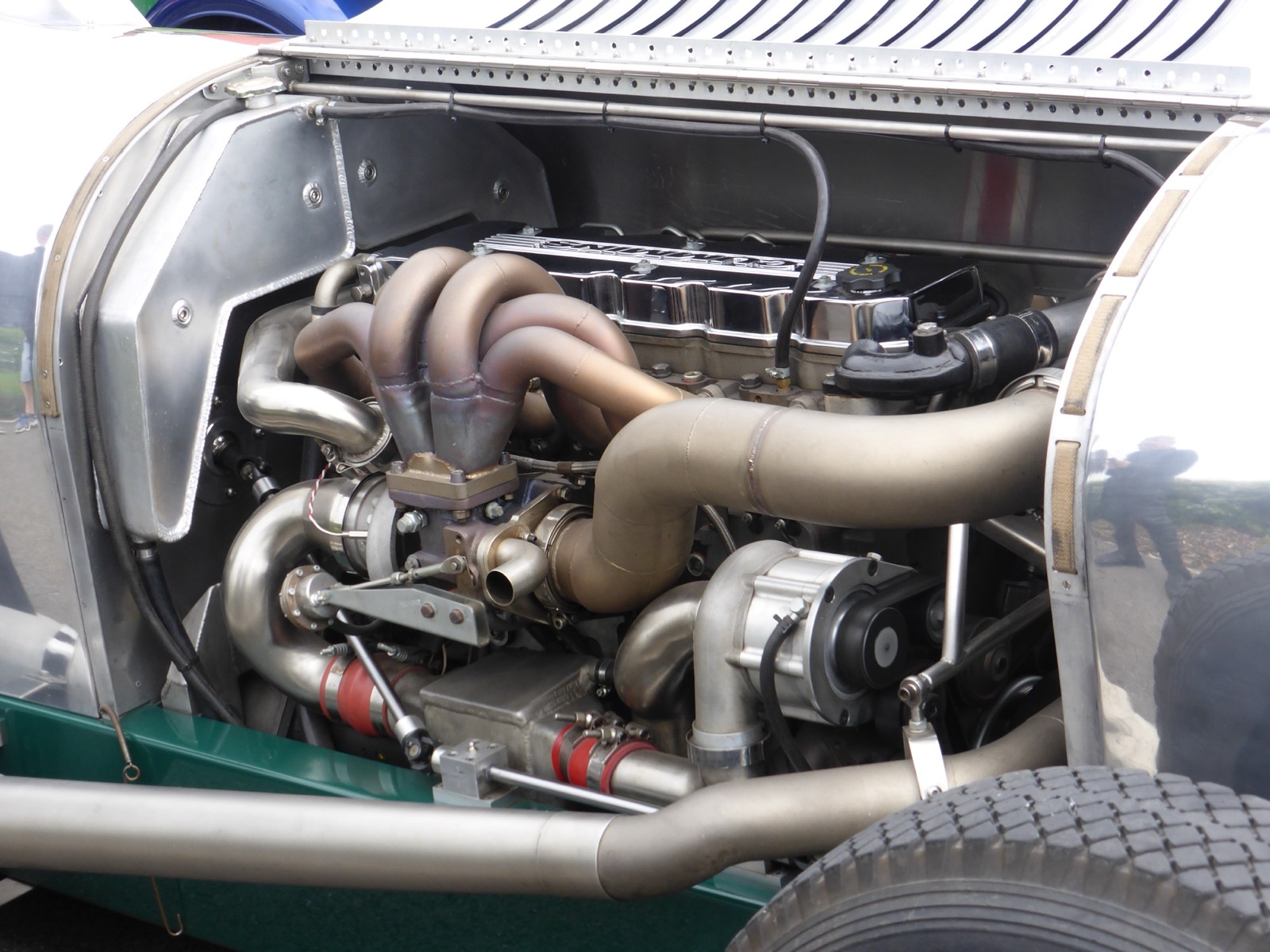 Engine bay of the Cummins Napier Railton replica, showing a six-cylinder diesel engine with polished exhaust pipes and a turbocharger inside an aluminium body